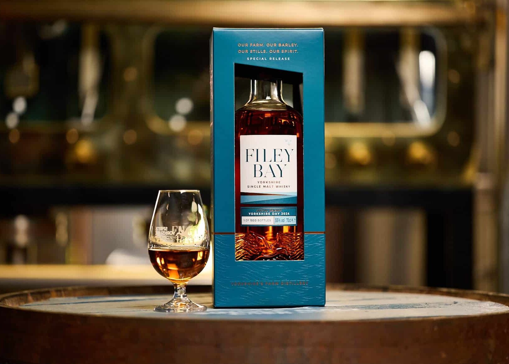A bottle of Filey bay Yorkshire Day 2024, with a glass next to it, sits on a cask with the Spirit ssafe behind in the beautiful new blue and copper Special Release carton